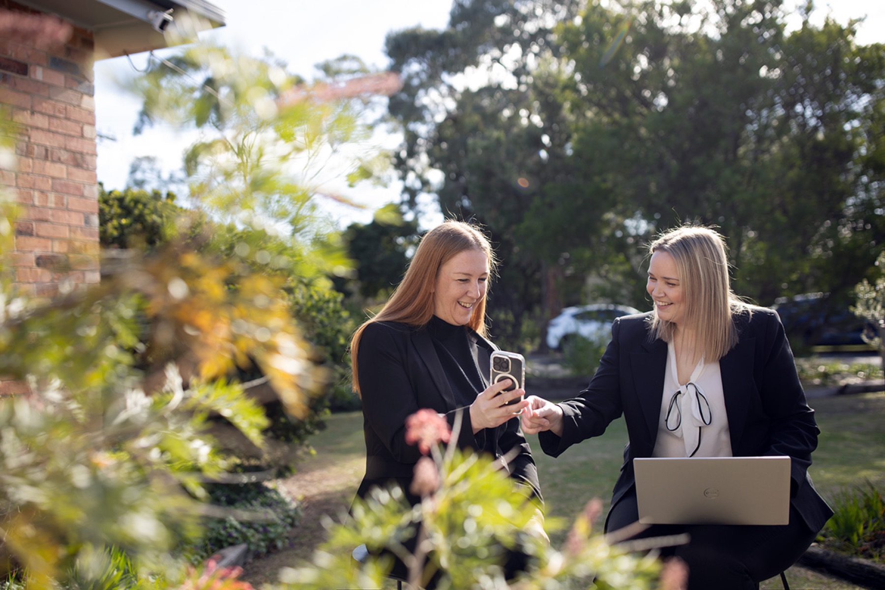 Two business colleagues collaborating with a laptop and phone outdoors