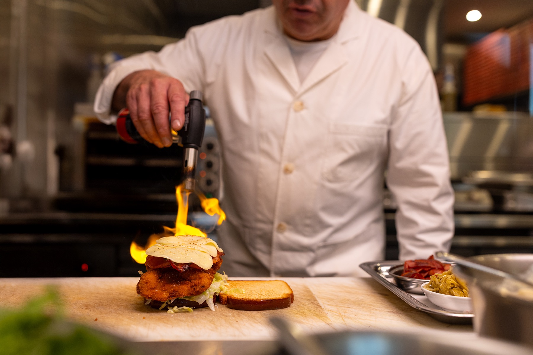Chef using a blowtorch while preparing a dish in a commercial kitchen